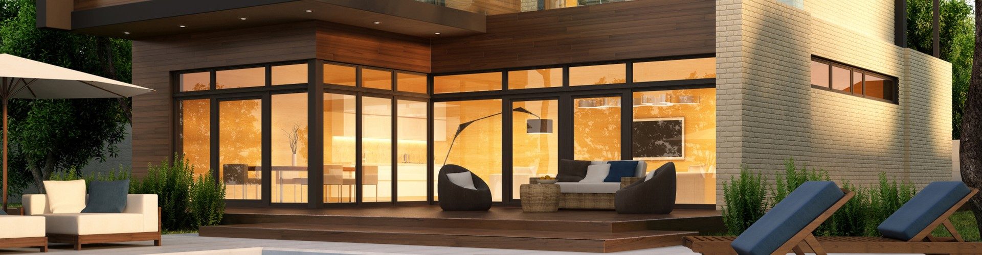 Stock photograph of a modern single-storey home at dusk, its floor-to-ceiling windows lit from inside, with a timber deck and outdoor seating